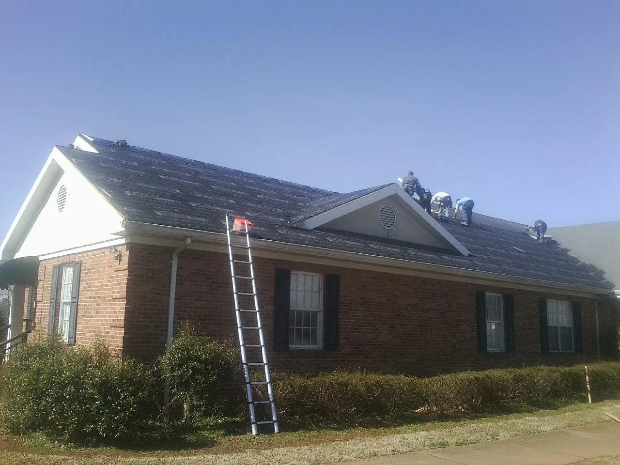 Crew tearing shingles off a brick ranch roof with a ladder set — Metal Roof Repair work by our crew in Vineland