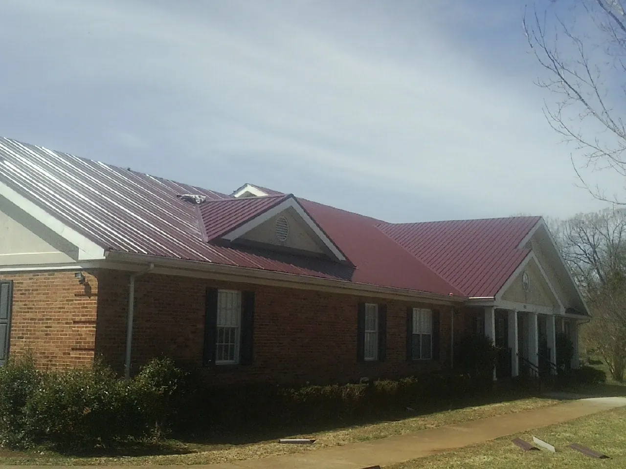 Red metal roof with gabled entries on a long brick building, from a Hail Damage Roof Repair job in Vineland