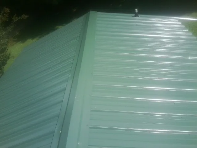 New green metal panels meeting at the ridge of a roof — Flat Roof Repair work by our crew in Vineland