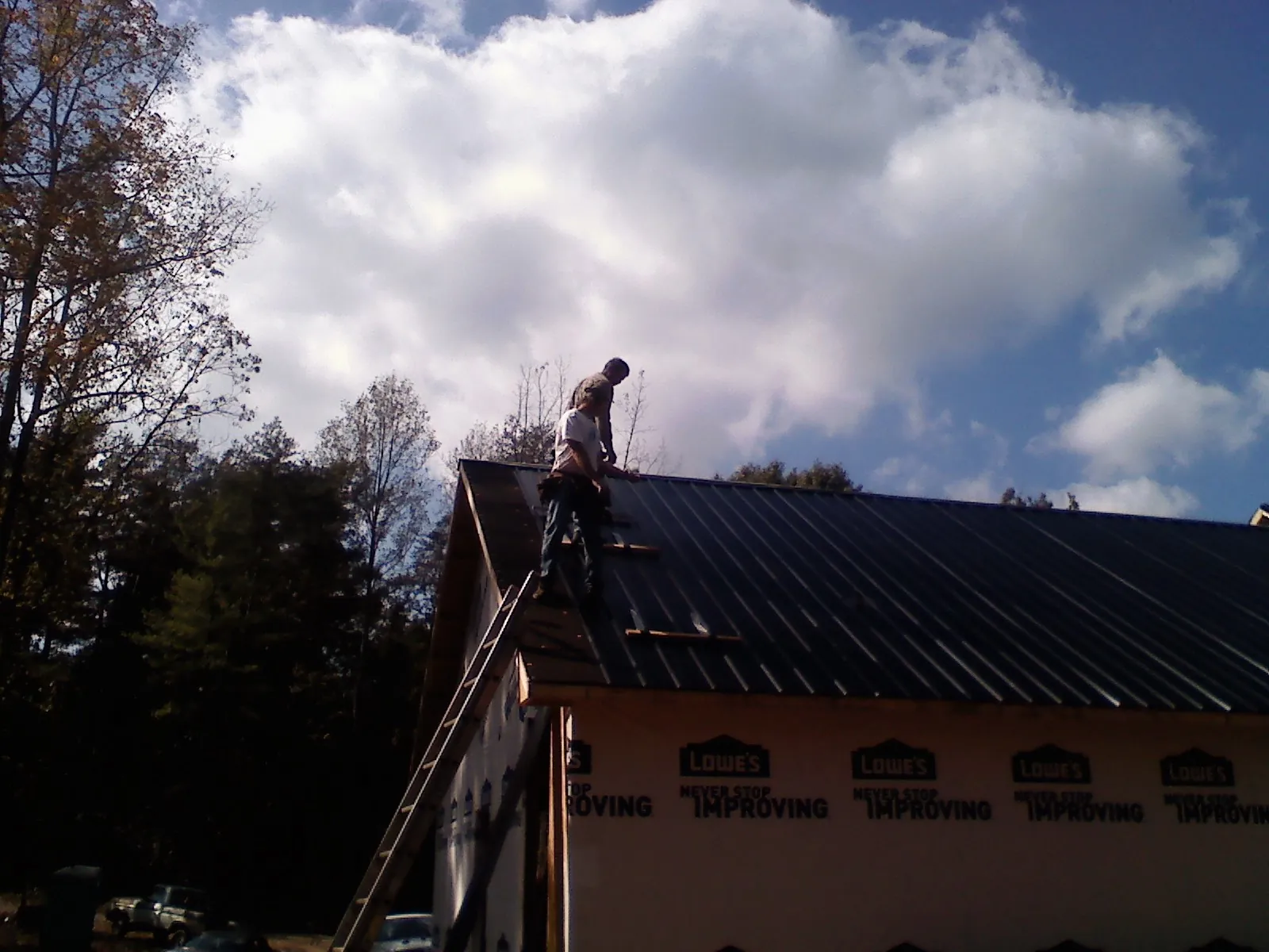 Roofer fastening dark metal panels high against a cloudy sky, from a Roof Inspection job in Vineland