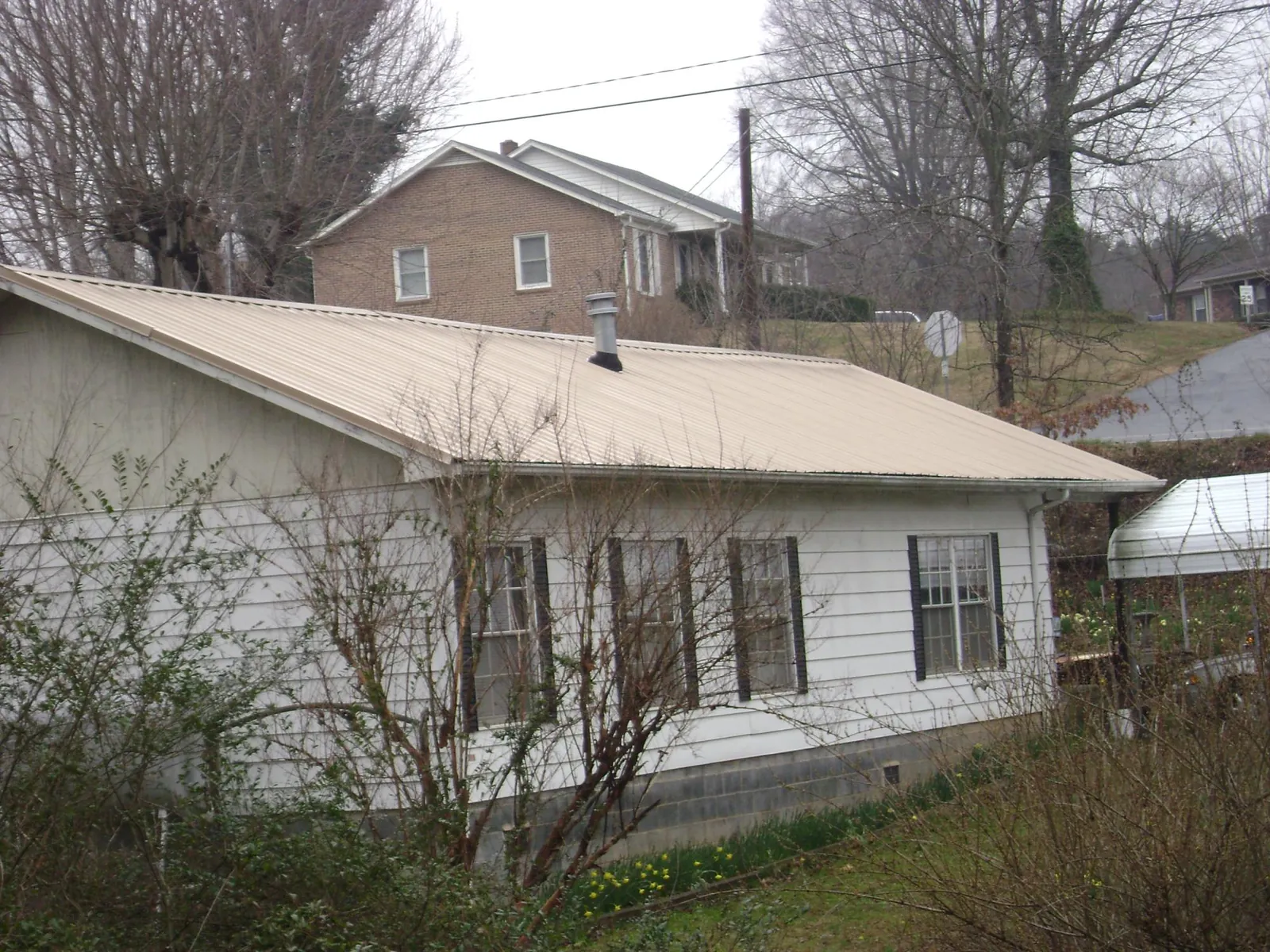 Tan metal roof on a white sided house set into a hillside — Commercial Roofing by Roofing Brothers in Vineland